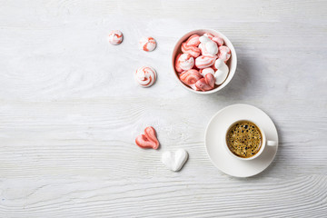 Beautiful romantic breakfast with coffee espresso and meringue cookies in the shape of hearts and candys. White cup stand on a wooden table. Flat lay with copy space.