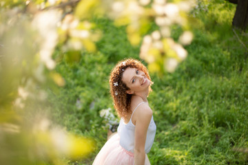 Naklejka na ściany i meble Young attractive girl walks in spring green park enjoying flowering nature