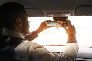 Driver adjusting rear view mirror in car