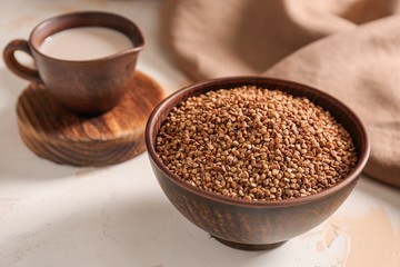 Bowl with raw buckwheat and jug of milk on table