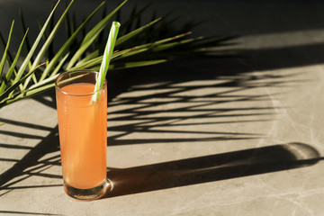 Summer cocktail concept with palm leaf and palm leaf's shade. A glass of fresh grapefruit tonic drink is on a grey marble background
