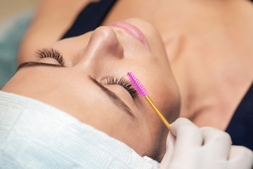 Obraz na płótnie Canvas Young woman receiving eyelash extension procedure in a beauty salon, close up.