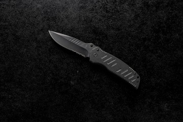 Closeup shot of an EDC pocket knife with a black handle on a black background