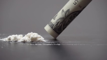 Drug Abuse. A rolled banknote snorting a line of cocaine powder. Problems with drugs concept. Grey background. Close-up macro shot.