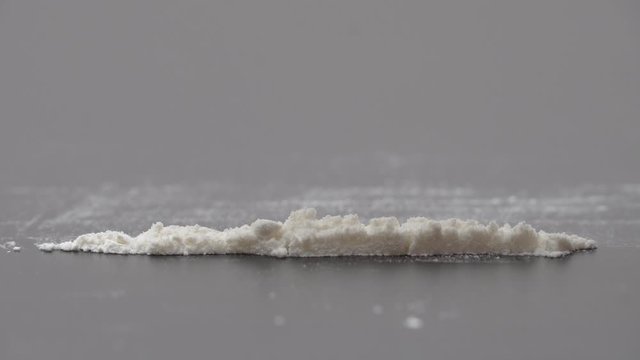 Drug Abuse. A rolled banknote snorting a line of cocaine powder. Problems with drugs concept. Grey background. Close-up macro shot.