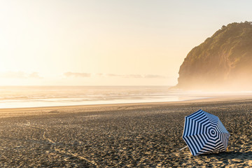 View of beach umbrella with white and blue stripes at Piha beach in evening light