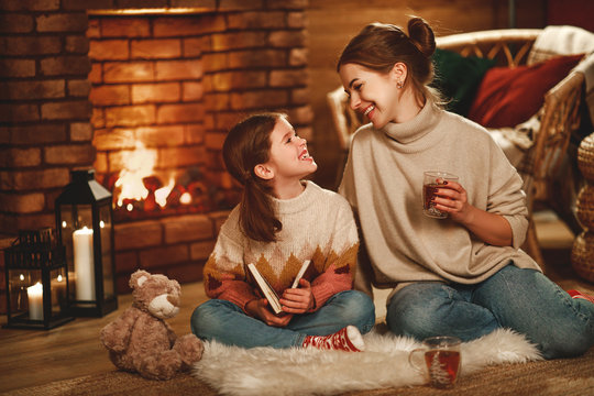family mother and child reading book and drink tea on winter evening by fireplace.