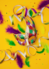 Festive, colorful mardi gras or carnivale mask and accessories over yellow background. Party...