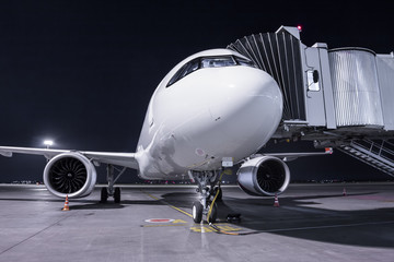 A white passenger airplane stands at the jetway connected to an external power supply on an airport night apron