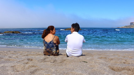 Young couple in love sitting together on the beach and looking at each other