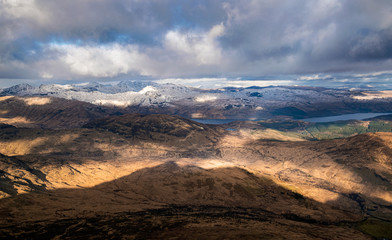 Dramatic winter view from Ben Lomond towards Loch Lomond and the peaks of Arrochar Alps in Scottish Highlands.
