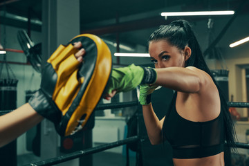 Athletic woman during fight training on boxing ring wearing green bandages on hands, punching...