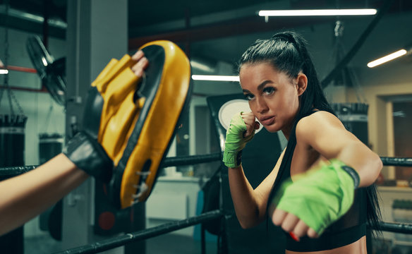 Athletic woman during fight training on boxing ring wearing green bandages on hands, punching exercises with coach