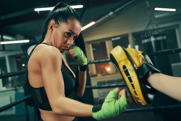 Fototapeta premium Athletic woman during fight training on boxing ring wearing green bandages on hands, punching exercises with coach