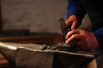 Fototapeta na wymiar Blacksmith hands hitting with hammer on a anvil using iron,steel, mettal molds