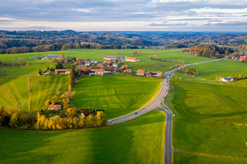 Aerial view Autumn landscape in Bavaria near Miesbach. Road going into the distance and the peaks of the Alps on the horizon. Yellow trees and green field