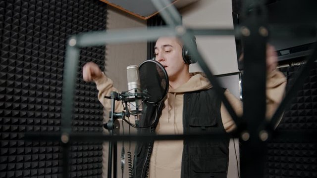 A man rapper recording his track in the studio actively gestures while the recording