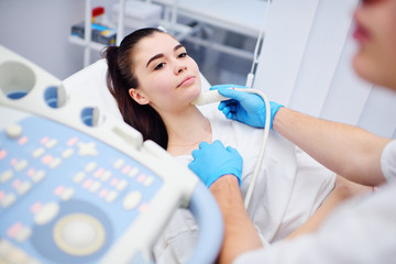 a young male doctor makes an ultrasound of the thyroid gland to a female patient.