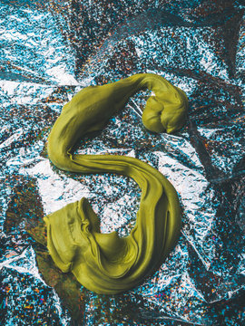 Letter S made from green slime on a aluminium foil shiny surface