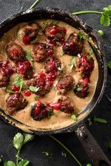Homemade savoury food. Beef meatballs in gravy with lingonberry sause and cilantro in black metal pan on black background