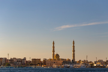 Fototapeta na wymiar Hurghada, Egypt, a city at sunset. View of the ancient city from the red sea. Panoramic view. A port with ships and a residential area with a mosque.