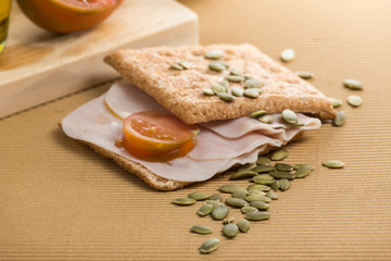 snack consisting of a sandwich of whole wheat bread and ham with tomato, pumpkin seeds dropped