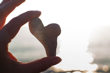 female hand holds a heart of natural stone against the background of the sea in the sun. Reminder...