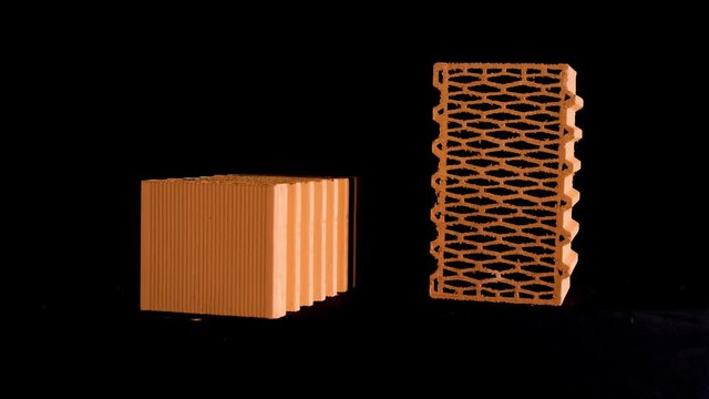 Two new perforated red bricks placed on black stand, building and construction materials concept. Stock footage. Bricks moving on black background.