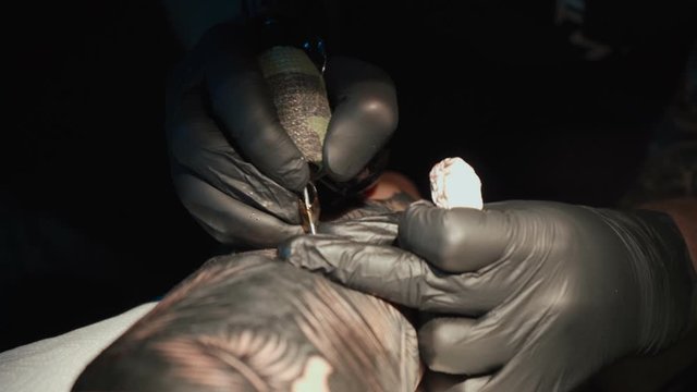 Close up video of man doing tattoo of snake on woman in studio