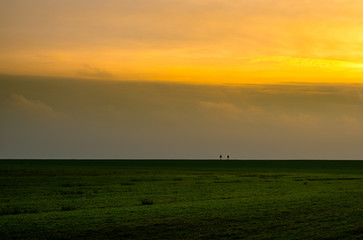 two people walking on Dutch dike in evening sky