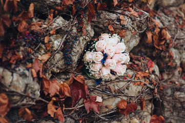 Wedding bouquet close-up of pink roses on a background of stones and autumn brown foliage and grapes. Photography, concept.