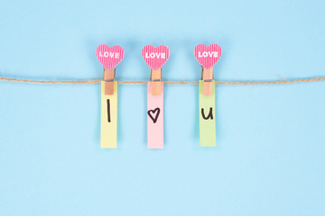 I love you concept. Close-up photo of three small wooden clothespins holding stickers with text isolated pastel color background