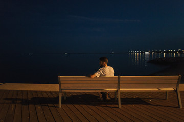 man sitting on a bench in a night city near the water
