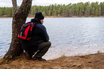 A man  in a forest near a lake with a backpack.