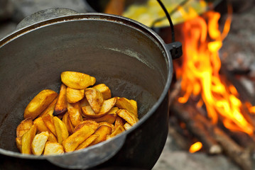 Potatoes are cooked in a large pot on fire. Food is cooked on a campfire in marching conditions.
