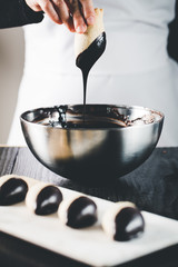 Woman hand dipping cookie in a melted dark chocolate.