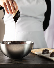 Woman hand dipping cookie in a melted dark chocolate.
