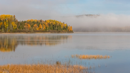 A lake in the forest in Canada, during the Indian summer, with fog on the water in the morning