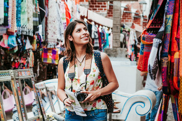 hispanic woman backpacker holding a map and camera in a traditional mexican Market in Mexico, Vacations