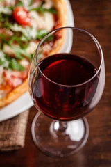 Fotobehang Italian food. Classic thin pizza with large sides, prosciutto, cherry tomatoes, arugula, parmesan cheese. Serving dishes in a restaurant on a white plate with red wine. © zukamilov
