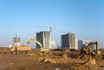 Excavator load the sand to the dump truck on construction site. Backhoe digs the ground for the foundation and construction of a new building. Background of the tower cranes