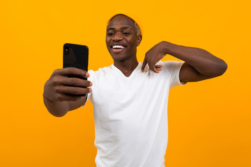 handsome black african man makes selfie on the phone on an orange background with copy space