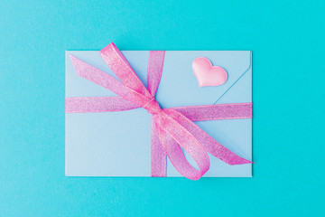 Envelope with pink bow and decorative heart on pastel blue background. Valentines day concept