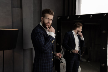 Handsome stylish man in blue suit in a cage at home standing on sofa near mirror. Holds his chin