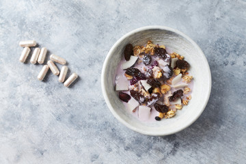 Bowl of granola with yogurt, nuts, cranberry and cocoanut. Sport supplements ( carnitine capsules ) in background. Bright stone  background. Top view. Copy space. 