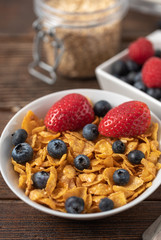 Healthy breakfast of cornflakes chips with blueberries and raspberries on dark desk.