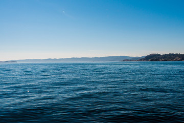Obraz premium View over small waves at sea with land in the horizon.