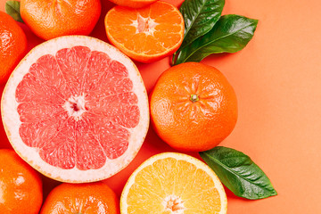 Fresh ripe mandarins, grapefruit and oranges with green leaves on orange background.