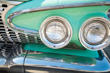 Full frame close-up of shiny chrome grill and headlights of mint green classic antique car
