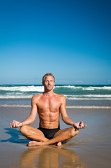 Fototapeta na wymiar Meditating man sitting cross-legged in lotus position on the shore of a wide tranquil beach